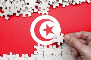 يد تضع قطعة أحجية فوق خلفية حمراء تحمل هلالاً ونجمة بيضاء، إشارة بصرية رمزية إلى علم تونس